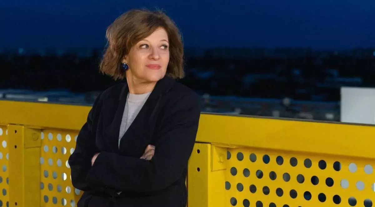 Vicepremierul Oana Gheorghiu în timp ce stă pe un balcon galben, poartă un sacou negru și privește în gol.