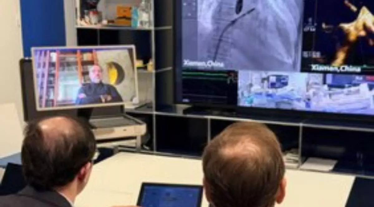 Doi medici privesc un ecran mare cu imagini dintr-o operație realizată în China și controlează procedura de la distanță, prin videoconferință și echipamente digitale.