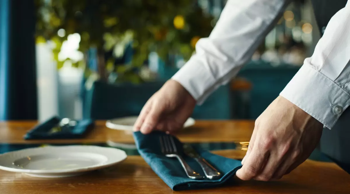 Un ospătar care așează un șervețel pe o masă