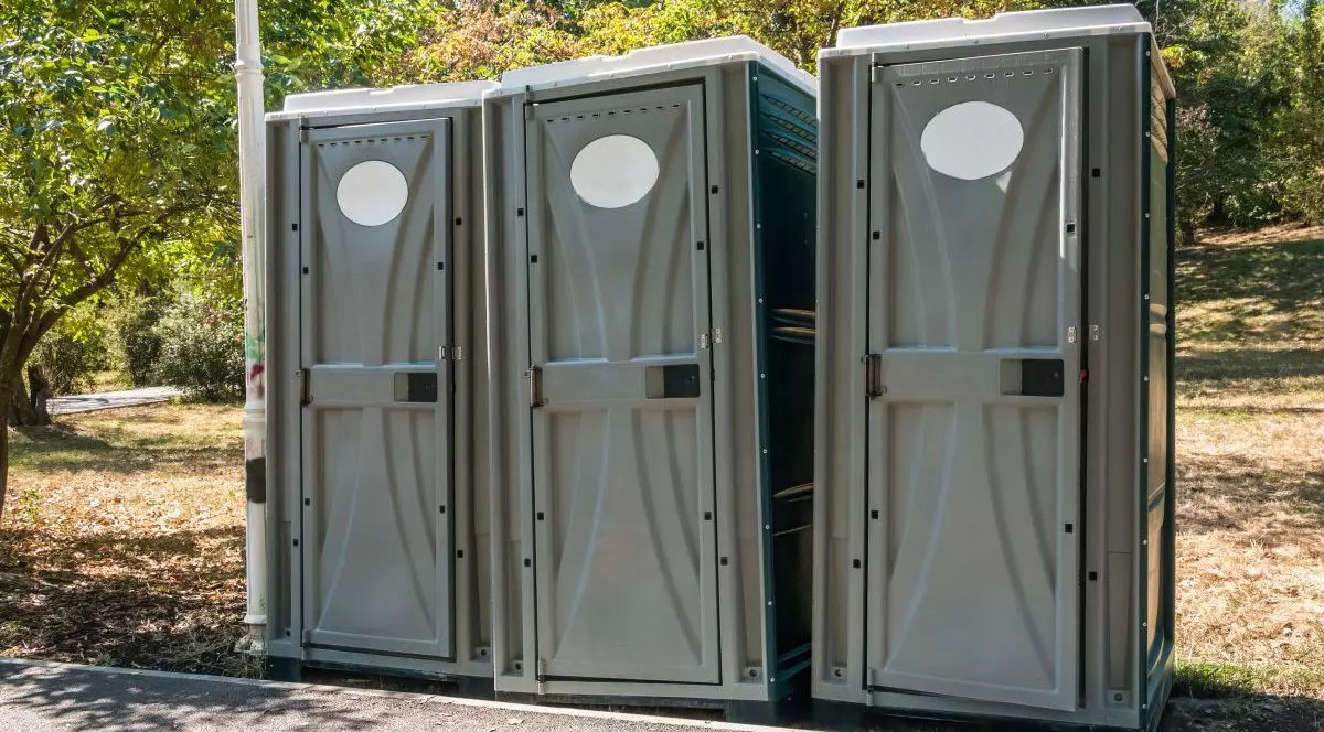 Trei toalete publice portabile sunt așezate într-o zonă verde din București, România.