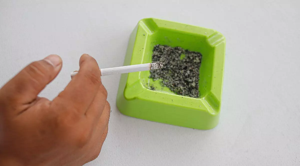 Țigară aprinsă într-o scrumieră verde pe fundal alb