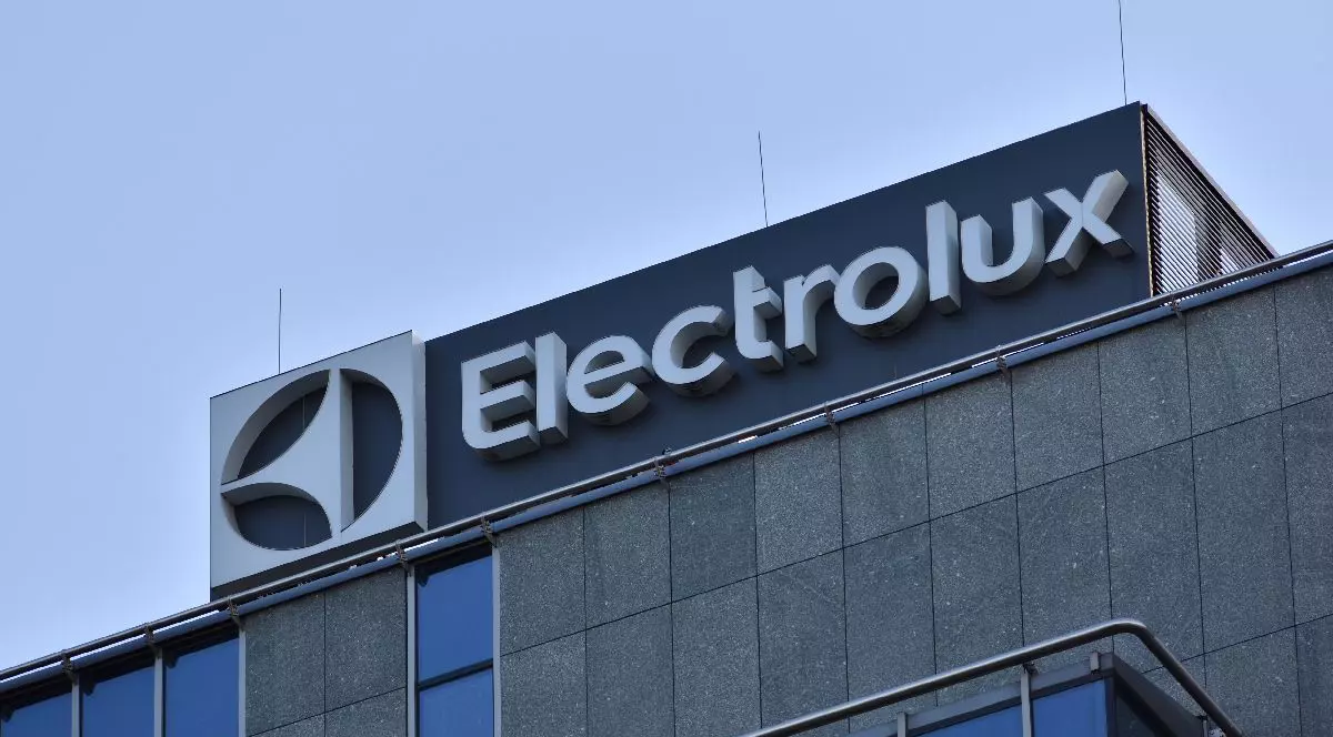 Fotografie a exteriorului unei clădiri de birouri cu logo-ul „Electrolux” în alb pe fond albastru închis. Fațada clădirii este compusă din panouri gri, texturate, cu ferestre din sticlă reflectorizantă.