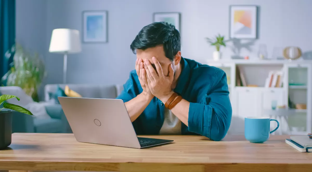 Un bărbat care stă la masă cu laptopul în față și cu capul în mâini, după ce a făcut cumpărături online