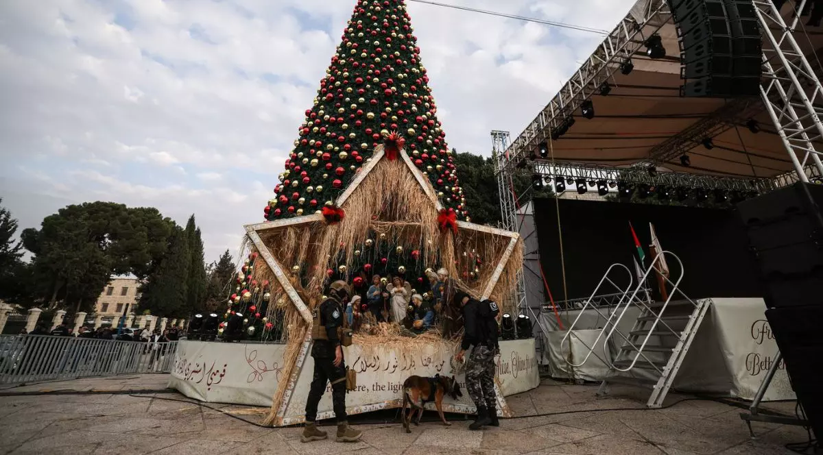 Un ofițer de poliție palestinian din unitatea K9 verifică decorațiunile de Crăciun înaintea ceremoniei de aprindere a luminilor din bradul de Crăciun din Betleem, în Cisiordania ocupată de Israel, pe 6 decembrie 2025.