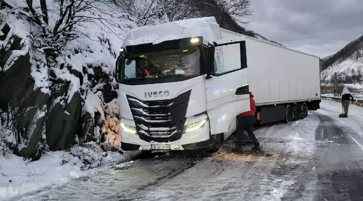 În imagine se vede un tir parcat pe marginea unei șosele acoperită cu zăpadă