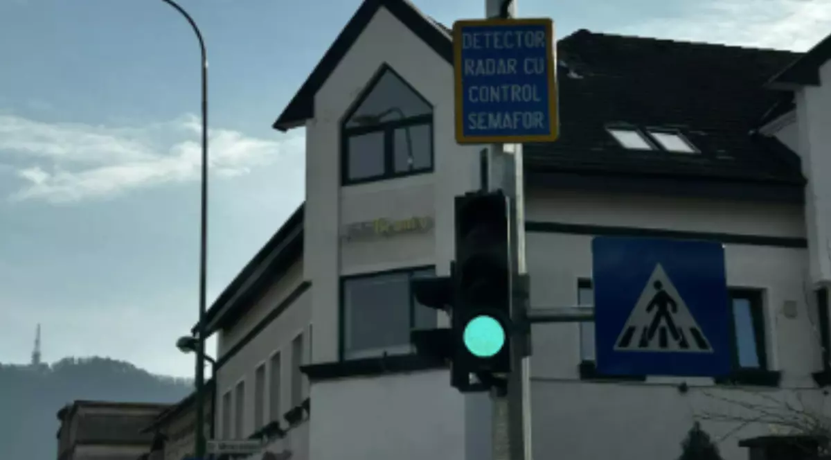 Un semafor care are culoare verde, iar deasupra este un panou pe care scrie Detector Radar cu Control Semafor