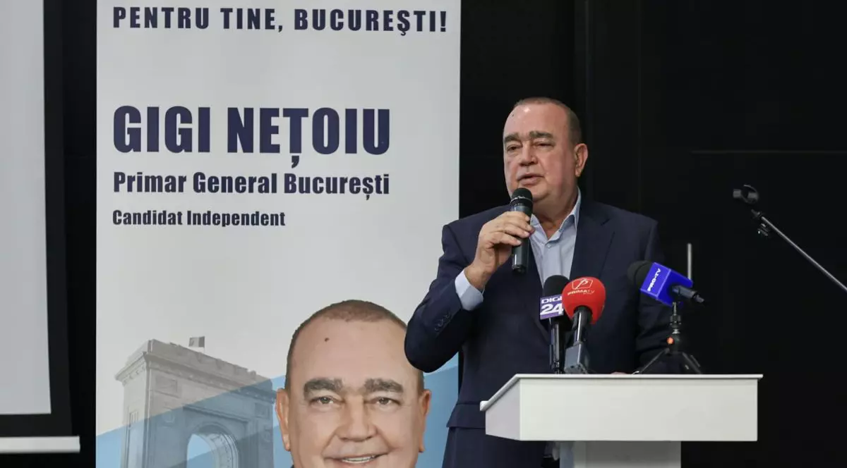 Gigi Nețoiu, vorbind la microfon la o conferință de presă, în fața unui banner cu numele său