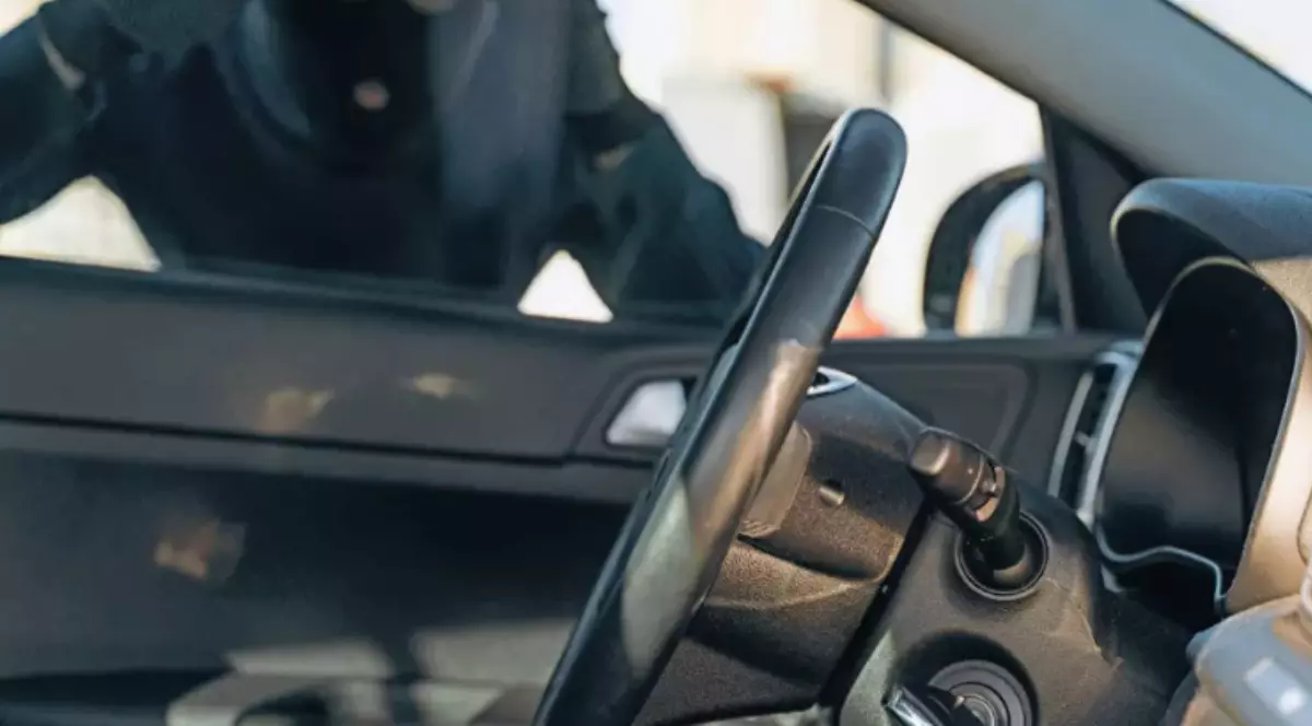 Un bărbat cu cagulă neagră care privește în interiorul unei mașini.