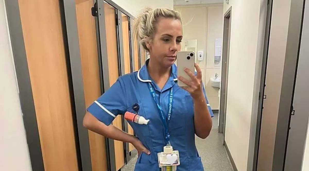 Meg Lynch, o asistenta din Marea Britanie, in uniforma albastra, cu ecuson la gat, isi face o poza in oglinda intr-o toaleta, se vad usi mari si o chiuveta in spate