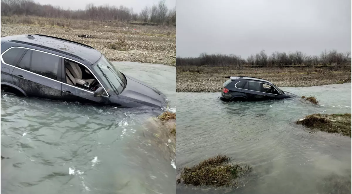 Mașina, un SUV de culoare închisă, a ajuns parțial scufundată în apă, după ce a ieșit de pe uscat și a alunecat în albia râului. Vehiculul este blocat pe jumătate în râu, în timp ce terenul din jur pare noroios și sălbatic, într-o zonă izolată.