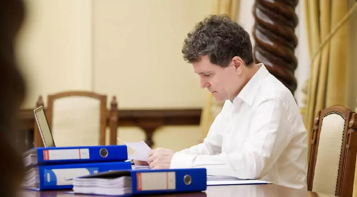 Nicușor Dan, stă la birou, în cămașă albă, și se citește niște documente. Pe birou sunt niște bibliorafturi albastre