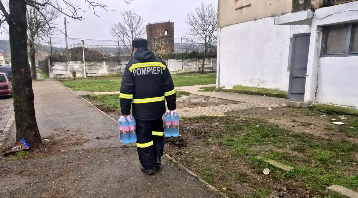 Imagine cu un pompier care duce sticle cu apă locuitorilor care nu mai au apă la robinet