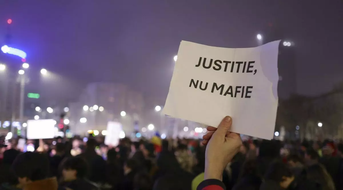 Un bărbat ține în mână o foaie pe care scrie „Justiție, nu mafie” la protestul din Piața Victoriei din 11 decembrie 2025