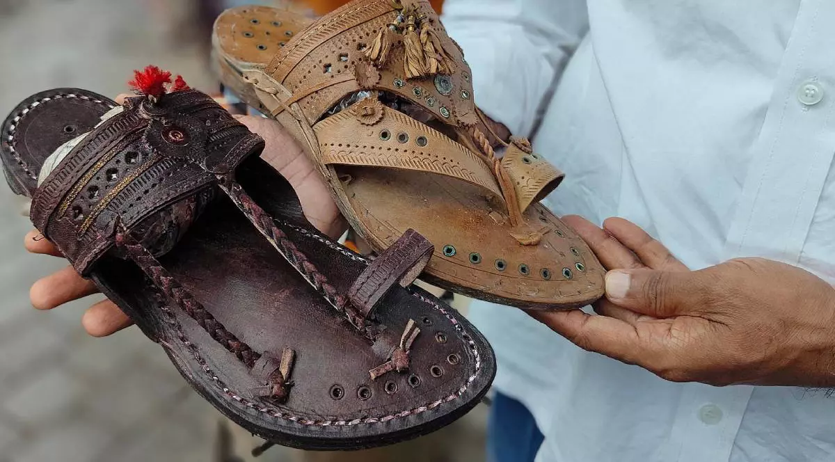 Un vânzător arată două sandale chappal-uri Kolhapuri , sandale indiene lucrate manual, una maro inchis alta maro deschis. iunie 2025