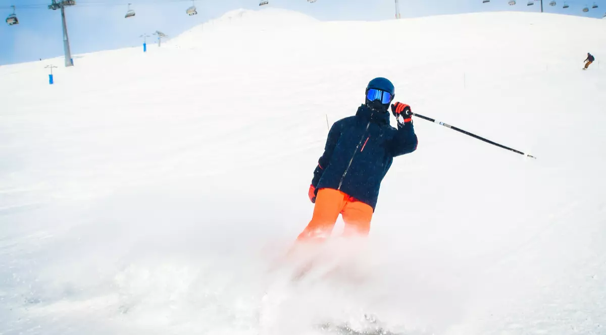 Un om îmbrăcat în echipament de schi negru cu portocaliu, pe pârtie.