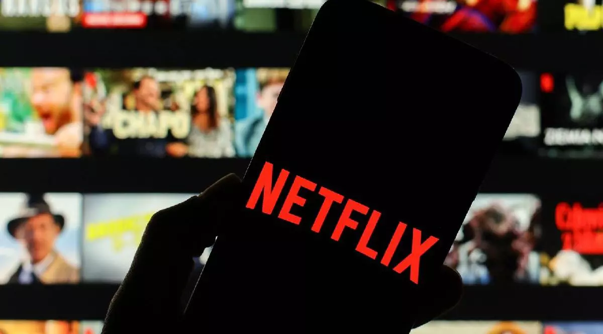 Sigla companiei Netflix afișată pe ecranul telefonului inteligent, cu ecranul de bun venit Netflix vizibil neclar în fundal