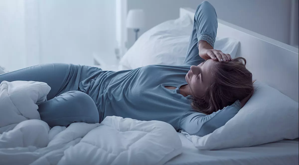 Femeie care stă în pat și are un somn neodihnitor