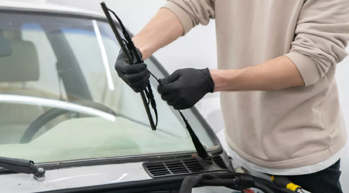 O persoană schimbă lamele ștergătoarelor de mașină în timp ce poartă mănuși pentru a asigura curățenia și siguranța într-un spațiu de lucru.