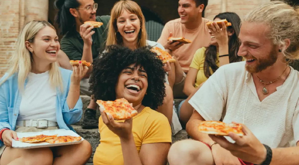 Prieteni zâmbitori din diverse culturi, mâncând pizza în aer liber