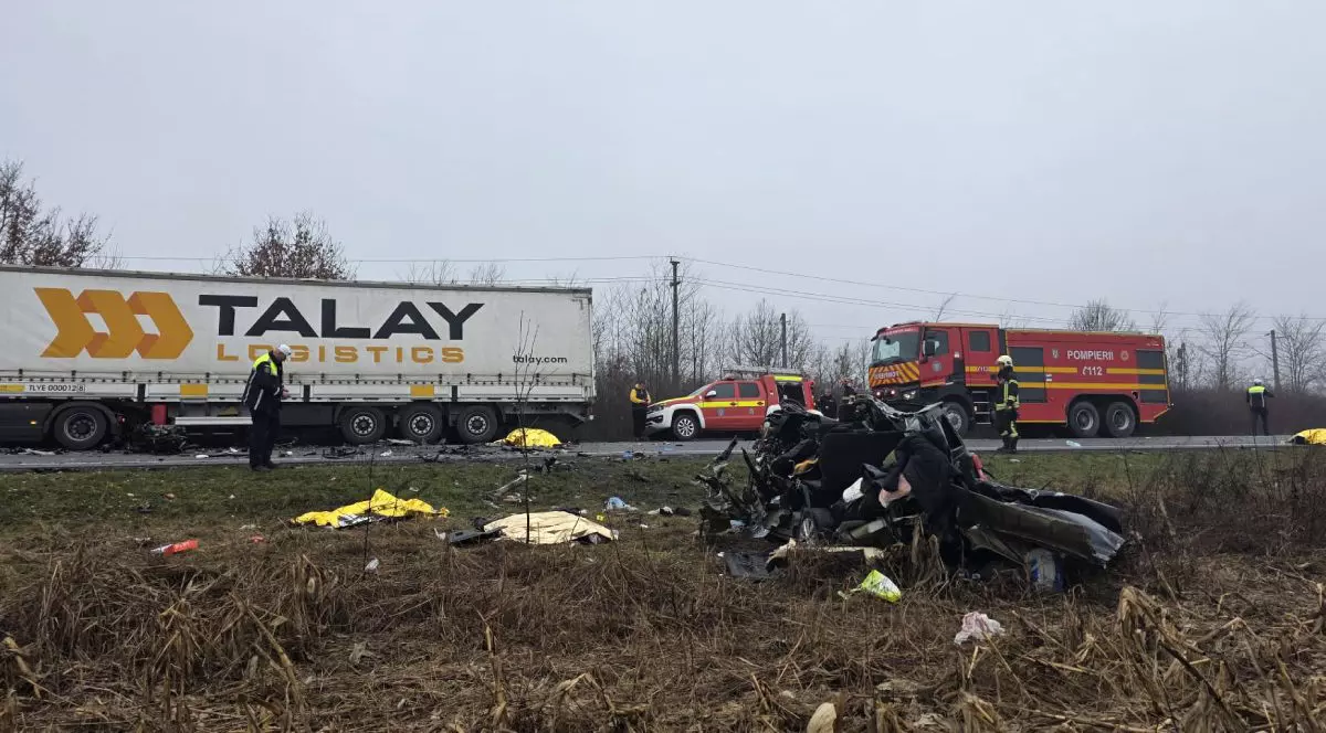 resturi de plastic și metal de culoare neagră așezate într-o grămadă uniformă pe marginea părții carosabile. în fundal se vede șoseaua, unde este parcată o autospecială de pompieri, o mașină de descarcerare și un Tir cu prelată albă