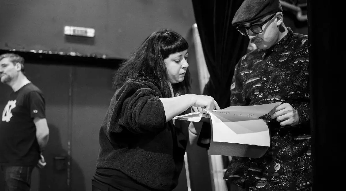 O fotografie alb negru cu regizoarea Alexandra Penciuc citind alături de un alt actor, probabil, scenariu piesei.