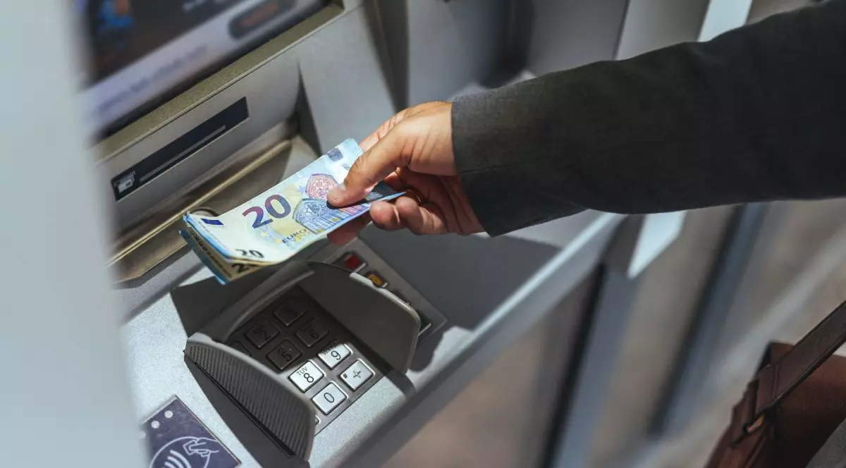 O persoană retrage bani, în bancnote de 20 de euro, dintr-un bancomat