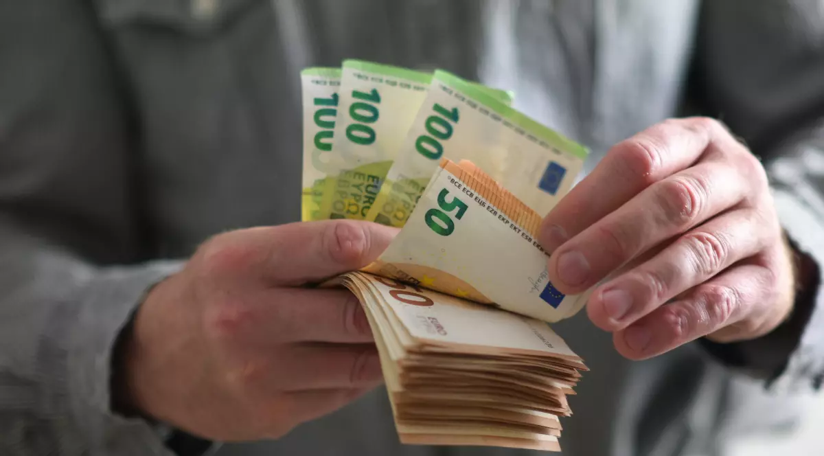 Un bărbat italian îmbrăcat cu o cămșă gri, în timp ce numără un teanc de bani. Hârtiile sunt de câte 50 și 100 de euro.