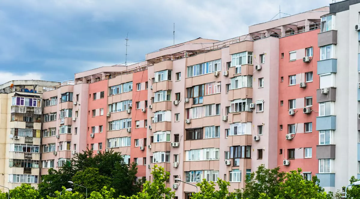 Mai multe blocuri de apartamente, cu fațade de culoare roz și crem, în București, cu copaci cu frunze verzi în față, în anul 2020