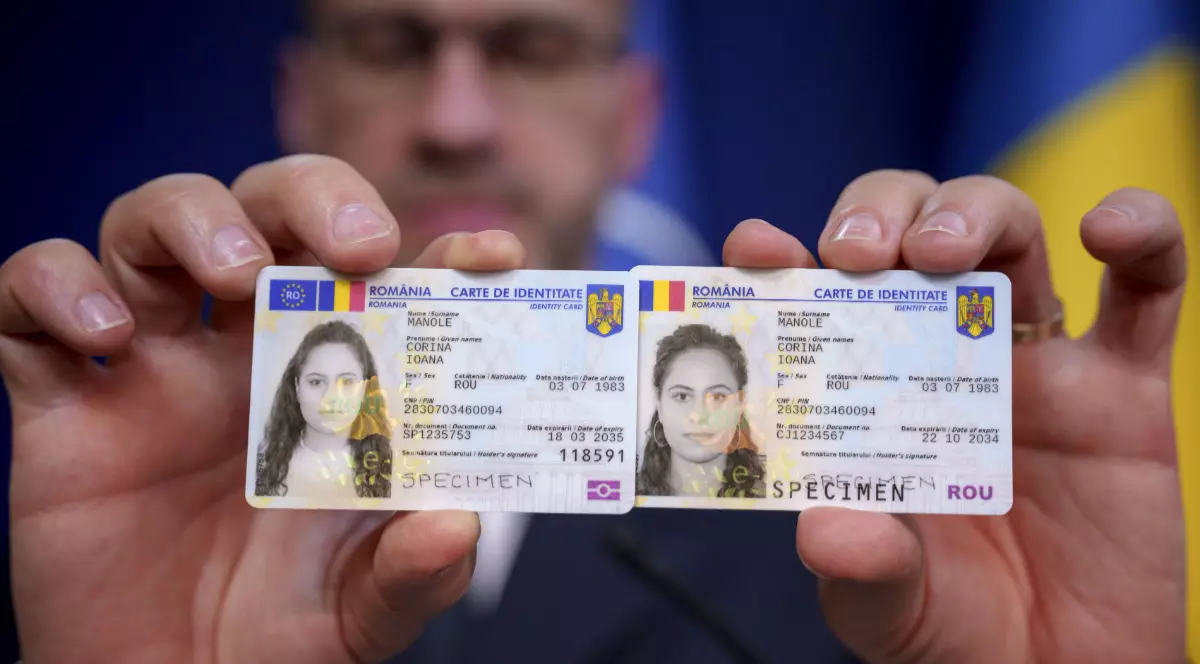 Un polițist care ține în mână două cărți electronice de identitate pe care le arată în fața camerei
