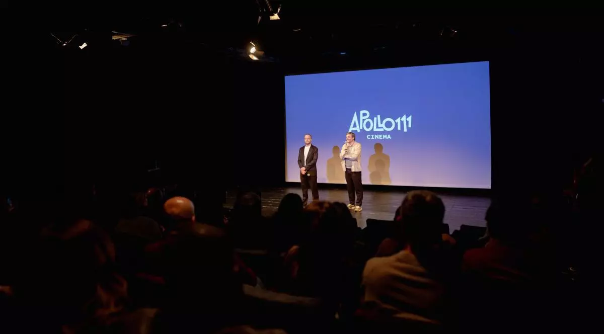 Doi bărbați sunt pe scenă la cinematograf, iar în spatele lor este proiectat pe un ecran mare numele cinematografului, Apollo111 Cinema, București