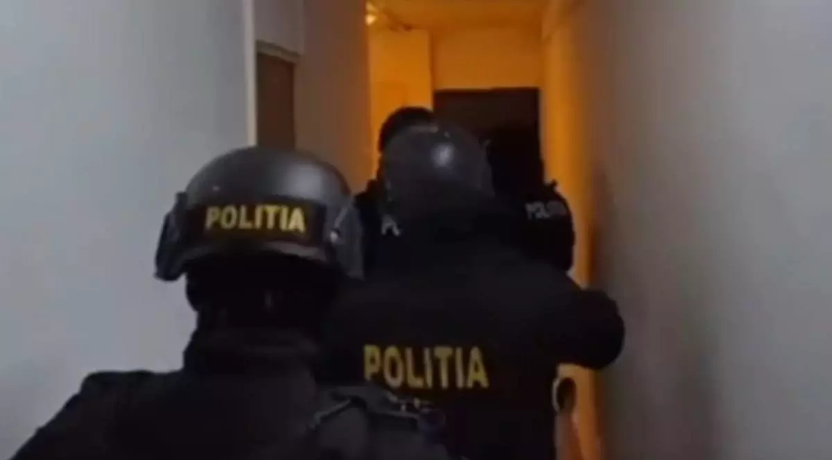 Mai multi politisti imbracati in negru, cu inscriptia Poliția pe uniforme, in timpul unei descinderi, inainteaza pe un hol
