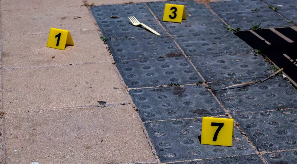 Trei marcaje galbene pentru locul crimei, pe un pavaj. Este o bucată de asfalt acoperită de un covor antiderapant albastru