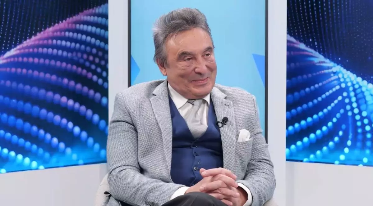 Dr. Ovidiu Grămescu în studioul emisiunii Bine pentru tine, îmbrăcat cu un sacou gri, o vestă albastră și cămașă albă, în timp ce stă pe un scaun