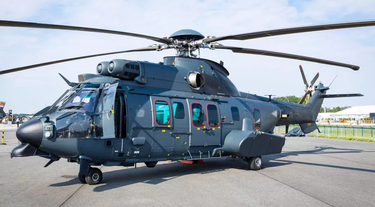 Un elicopter Airbus H225M, la sol, de culoare gri închis și negru, cu palele întinse