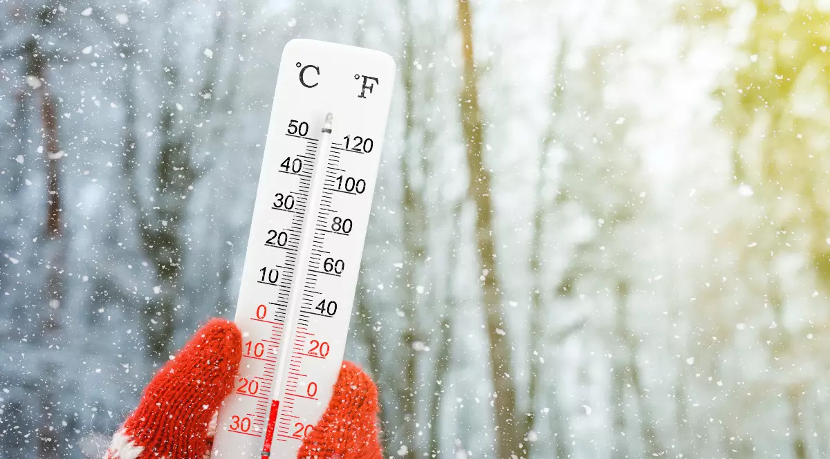 Imaginea surprinde un termometru care indică temperaturi negative, ținut de o mână cu mănușă, în timp ce ninge abundent. Fotografia sugerează ger puternic și condiții de iarnă severă.