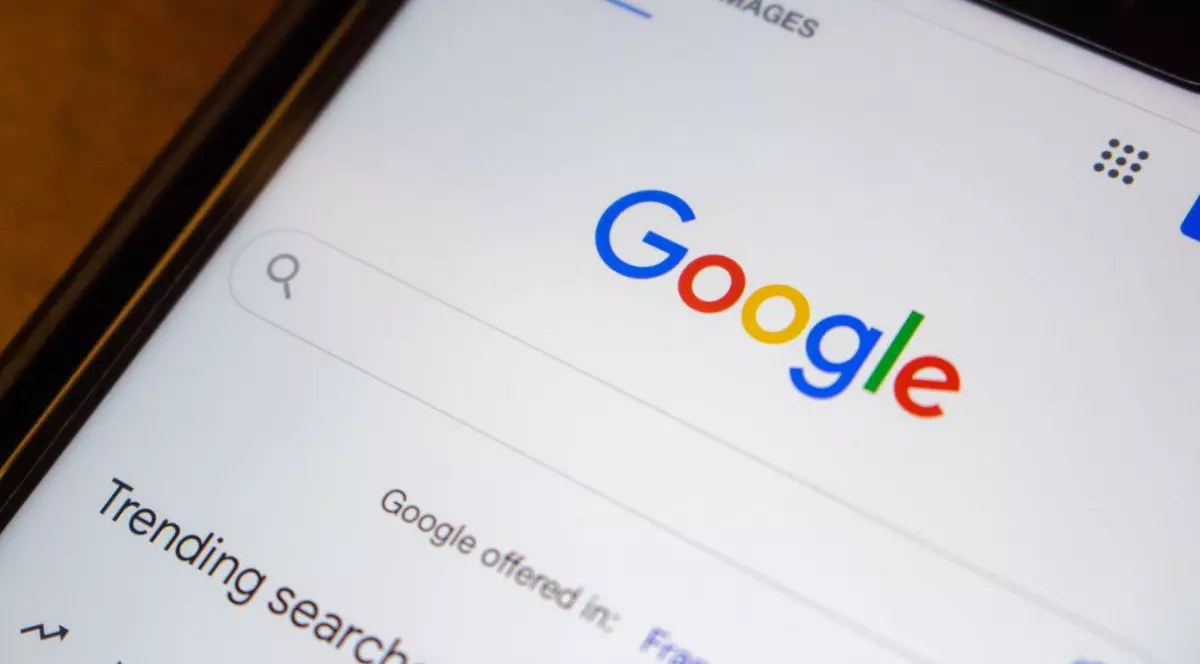 Logo-ul site-ului Google.com în prim-plan pe un iPhone așezat pe o masă de lemn.