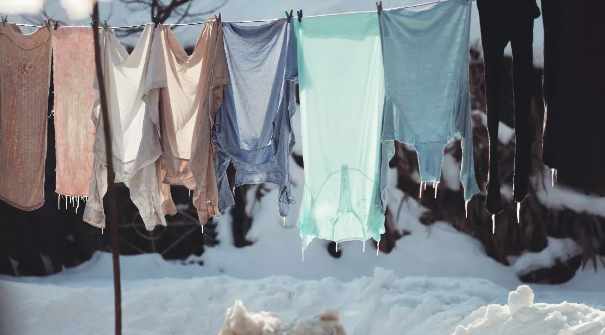 Haine puse la uscat pe sârmă, afară, pe timp de iarnă, acoperite cu gheață și zăpadă pe fundal și pe jos