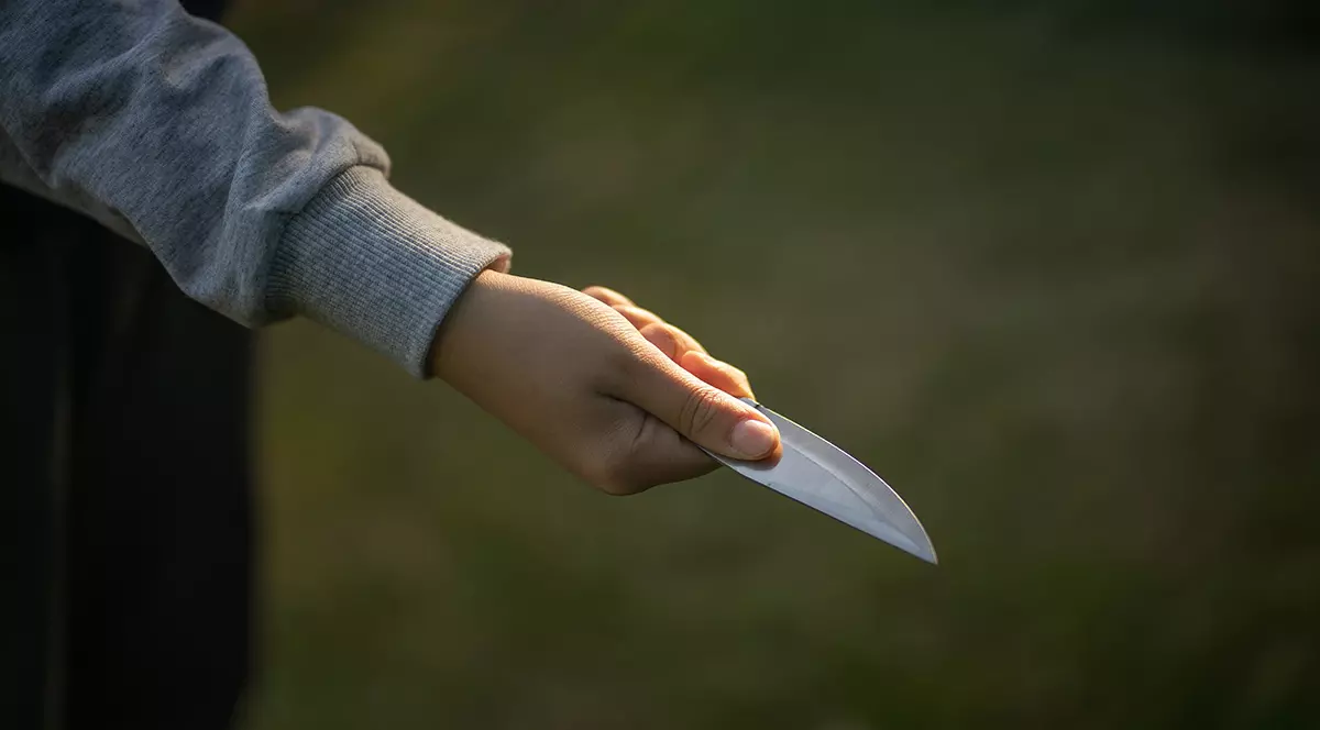O imagine cu o mână de copil care ține în mână un cuțit pentru a ilustra o crimă.