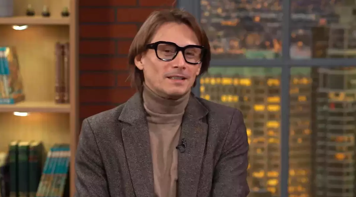 Actorul Marius Manole, in studioul podcastului Prima Data. Manole poarta o maletă maro deschis si un sacou de culoare inchisa cu picățțele