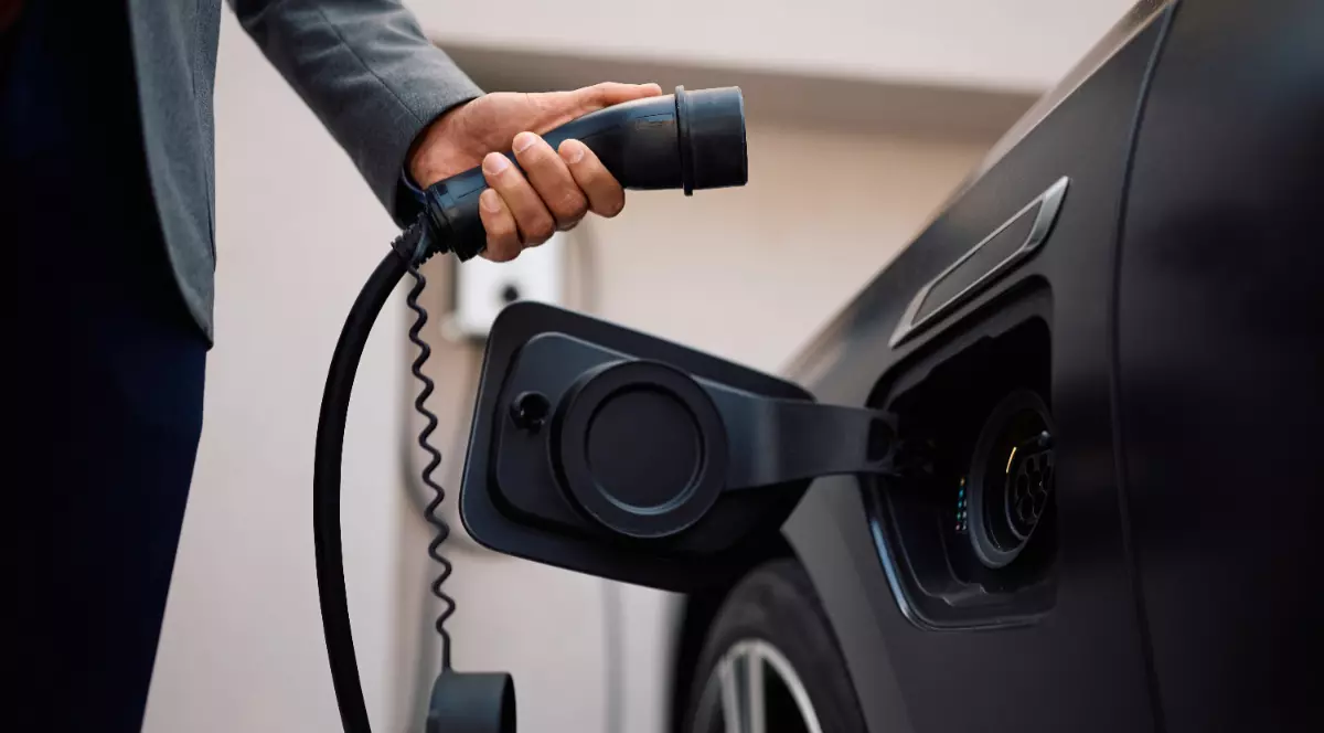 Un bărbat îmbrăcat în negru, în timp ce pune o mașină electrică la încărcat