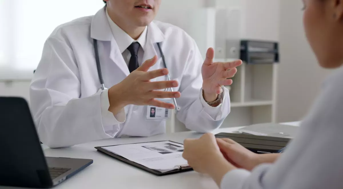 Un medic discuta intr-un cabinet, la masa cu un pacient