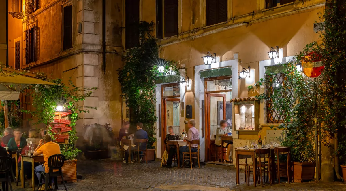 Un restaurant din Italia, în timpul serii, mesele sunt așezate la intrare, turiștii sunt la mesele așezate pe drumurile de piatră