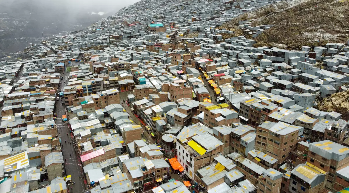 Imaginea surprinde un cartier extrem de dens construit, cu mii de locuințe improvizate înghesuite pe versanții unui deal arid. Casele din cărămidă și tablă se întind până la orizont, creând un peisaj urban haotic, marcat de sărăcie și condiții de trai dificile.