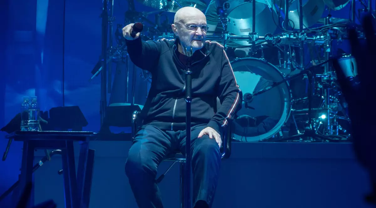 Phil Collins cântă așezat pe un scaun