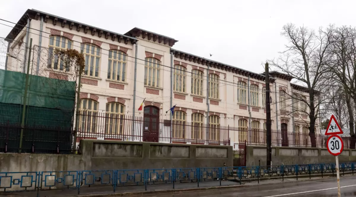 O școală situată la marginea unei străzi prevăzute cu indicatoare rutiere de avertizare și un gard metalic de protecție, în Galați.
