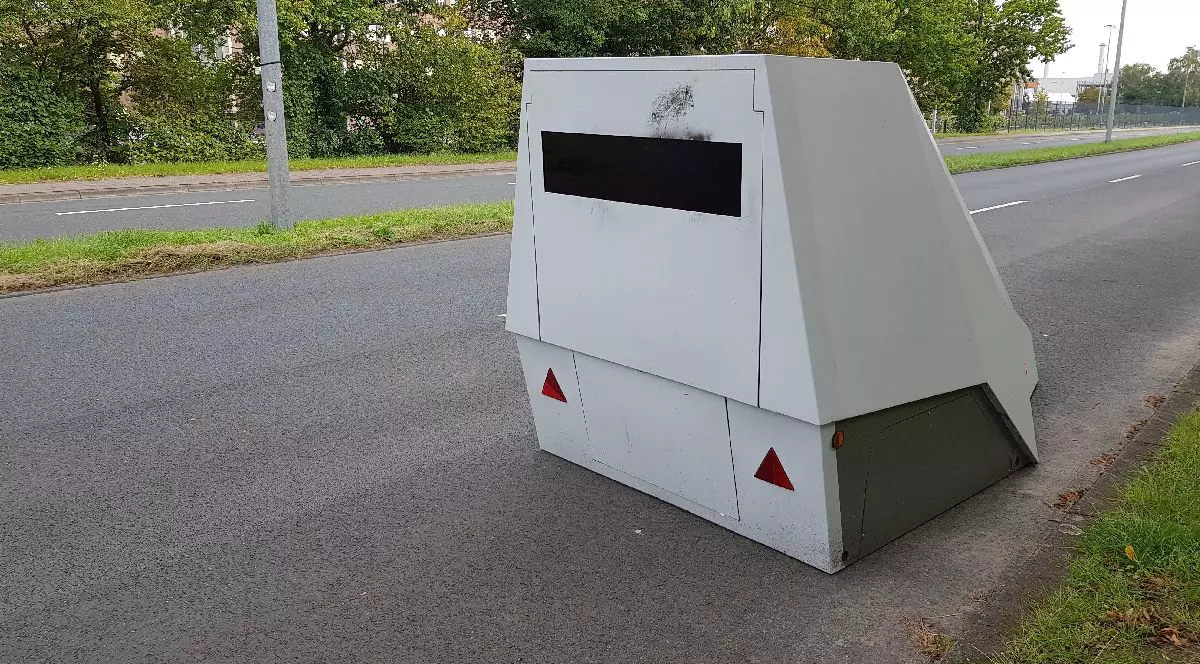 Fotografie a unui radr fix situată pe o stradă, cu verdeață și copaci de o parte și de alta a drumului asfaltat.