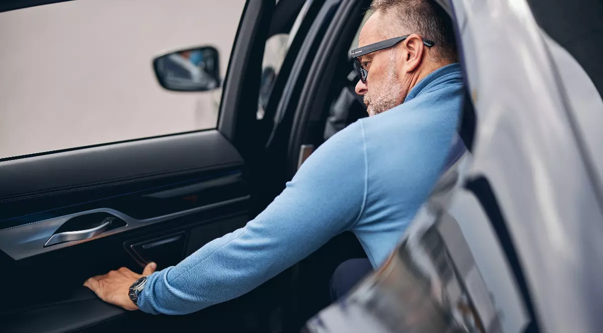 Imaginea arată un bărbat care coboară dintr-o mașină, surprins din spate, în timp ce deschide portiera din interior. Scena sugerează un moment obișnuit de ieșire dintr-un autoturism, fără elemente care să identifice persoana sau contextul exact.