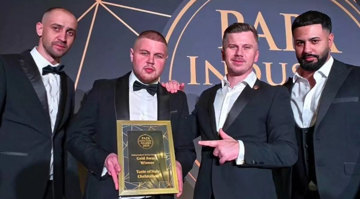 In imagine 4 barbati , imbracat elegant in costume negre camasi albe, la ceremonia PAPA Awards din Anglia, In mijloc se afla Cosmin Stoian, sef pizzar la Taste of Italy, care tine in maini o placeta cu premiu, si Sergiu Teacu, patroul localului, cu mana dreapta pe umarul lui Cosmin si cu degetul aratator de la mana stanga arata spre premiu. Langa ei, stanga dreapta, alti doi barbati tineri