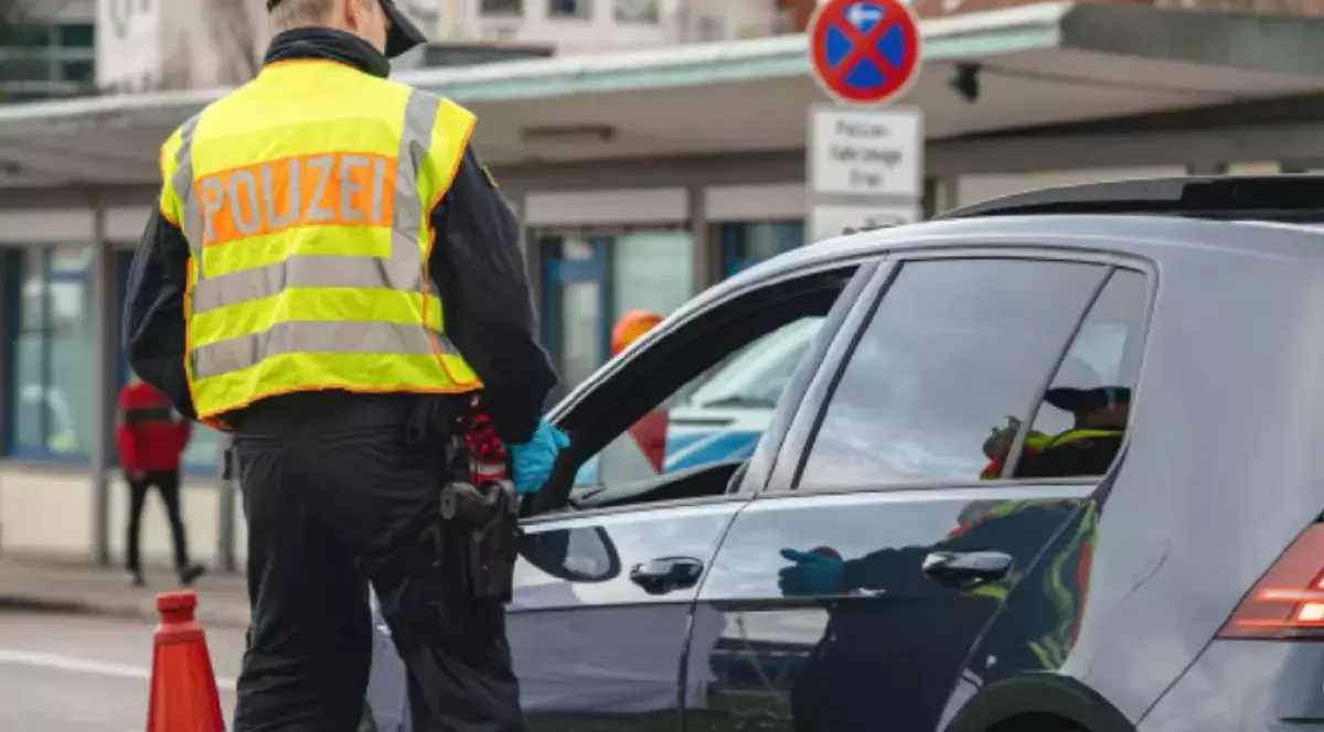 Un polițist care poartă vestă reflectorizantă pe care scrie Polizei. Acesta a oprit un șofer cu mașină neagră.