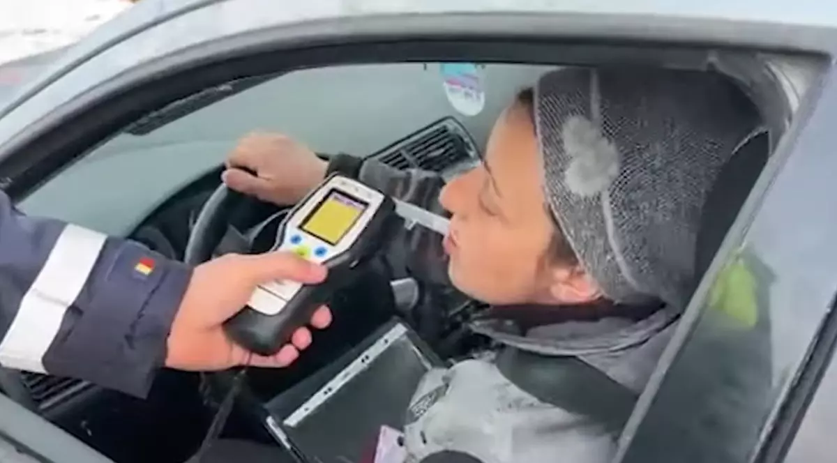Fotografie cu o femeie purtând o căciulă gri, suflând în etilotest, într-o mașină.